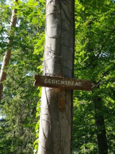 Wegweiser mit der Richtung zum Gedichtpfad an einem Baumstamm